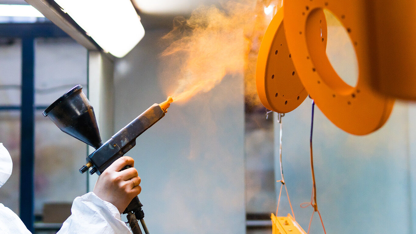 A worker paints manufactured parts with a spray gun